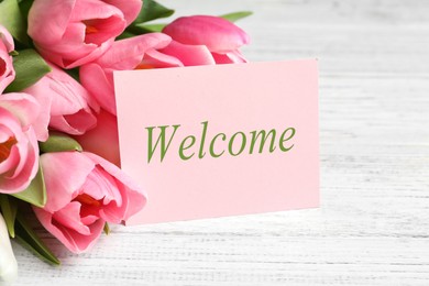 Image of Welcome card and beautiful pink tulips on white wooden table, closeup