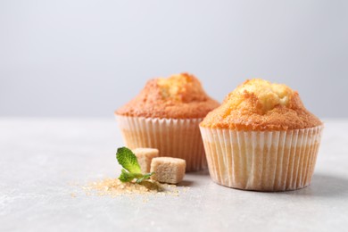 Photo of Delicious sweet muffins and brown sugar on light grey textured table, closeup. Space for text