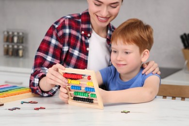 Photo of Happy mother and son playing with abacus at white marble table in kitchen, focus on game kit. Learning mathematics with fun