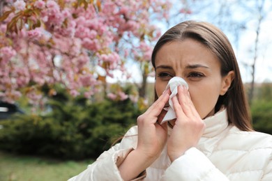 Photo of Woman suffering from seasonal pollen allergy near blossoming tree outdoors