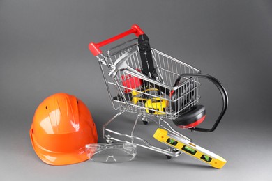 Photo of Small shopping cart with set of construction tools. protective glasses and hard hat on grey background