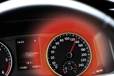Image of Speedometer on car dashboard and red light around it, closeup