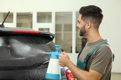 Photo of Worker spraying water onto car window before tinting