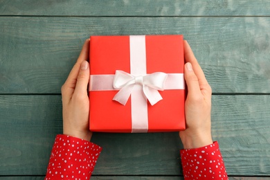 Photo of Woman holding gift box at wooden table, top view. Valentine's Day celebration
