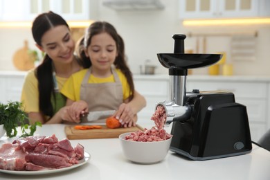 Photo of Mother and little girl cutting carrot in kitchen, focus on meat grinder