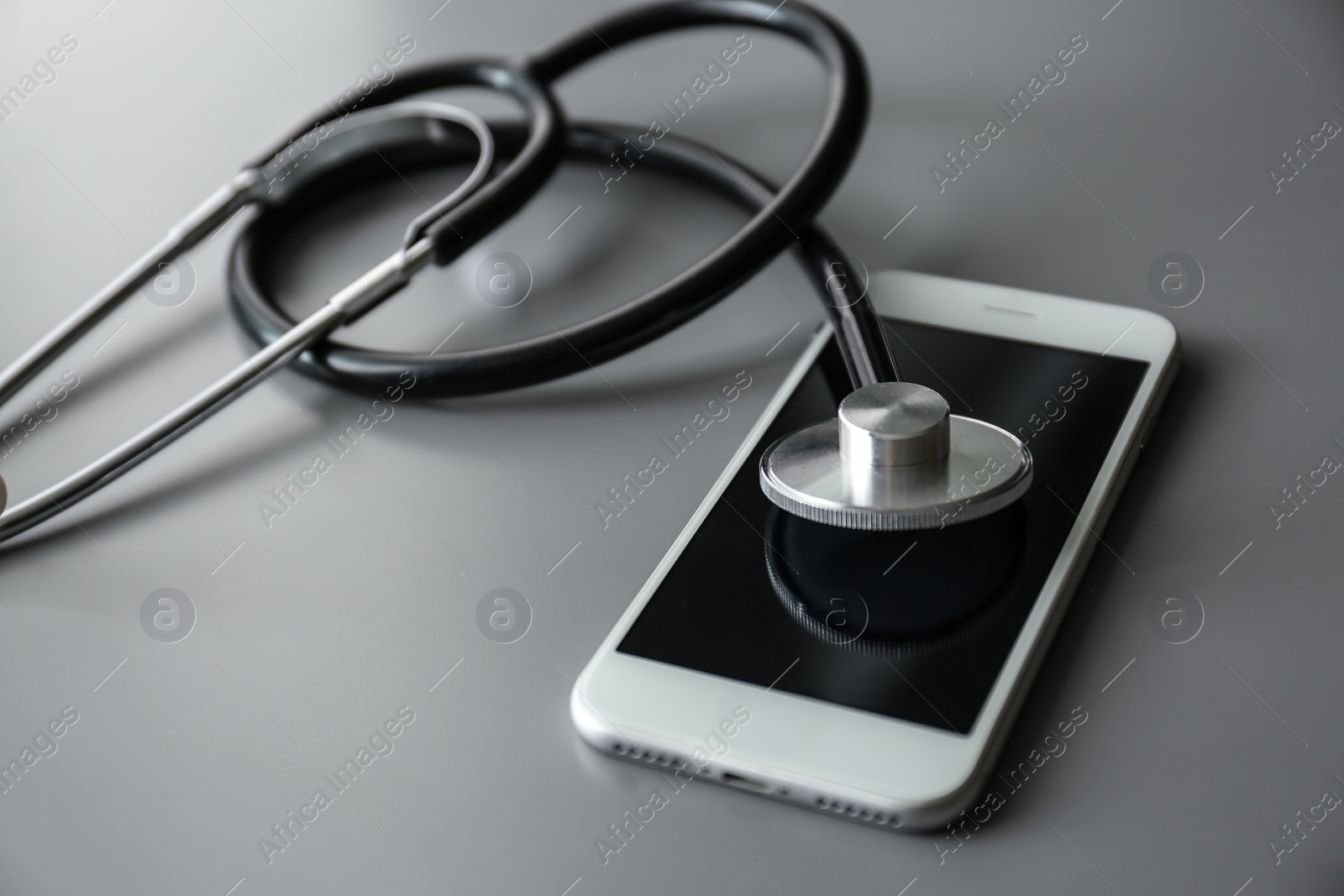 Photo of Smartphone and stethoscope on grey table, closeup with space for text. Repairing service