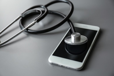Smartphone and stethoscope on grey table, closeup with space for text. Repairing service