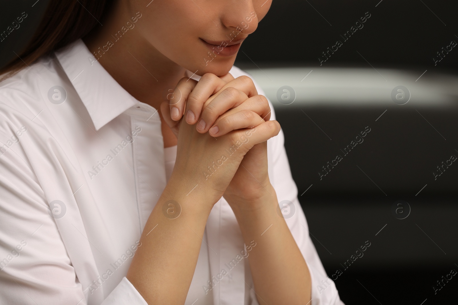 Photo of Religious woman with clasped hands praying indoors, closeup