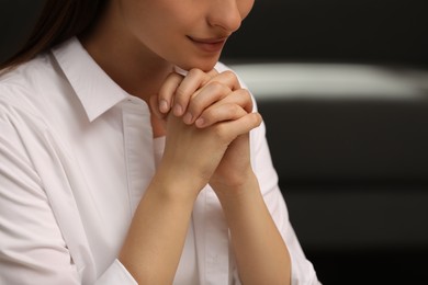 Religious woman with clasped hands praying indoors, closeup