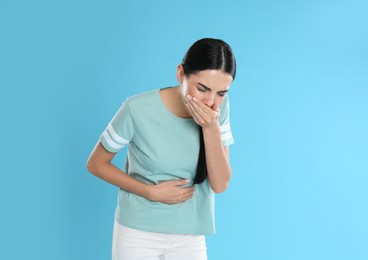 Woman suffering from stomach ache and nausea on light blue background. Food poisoning