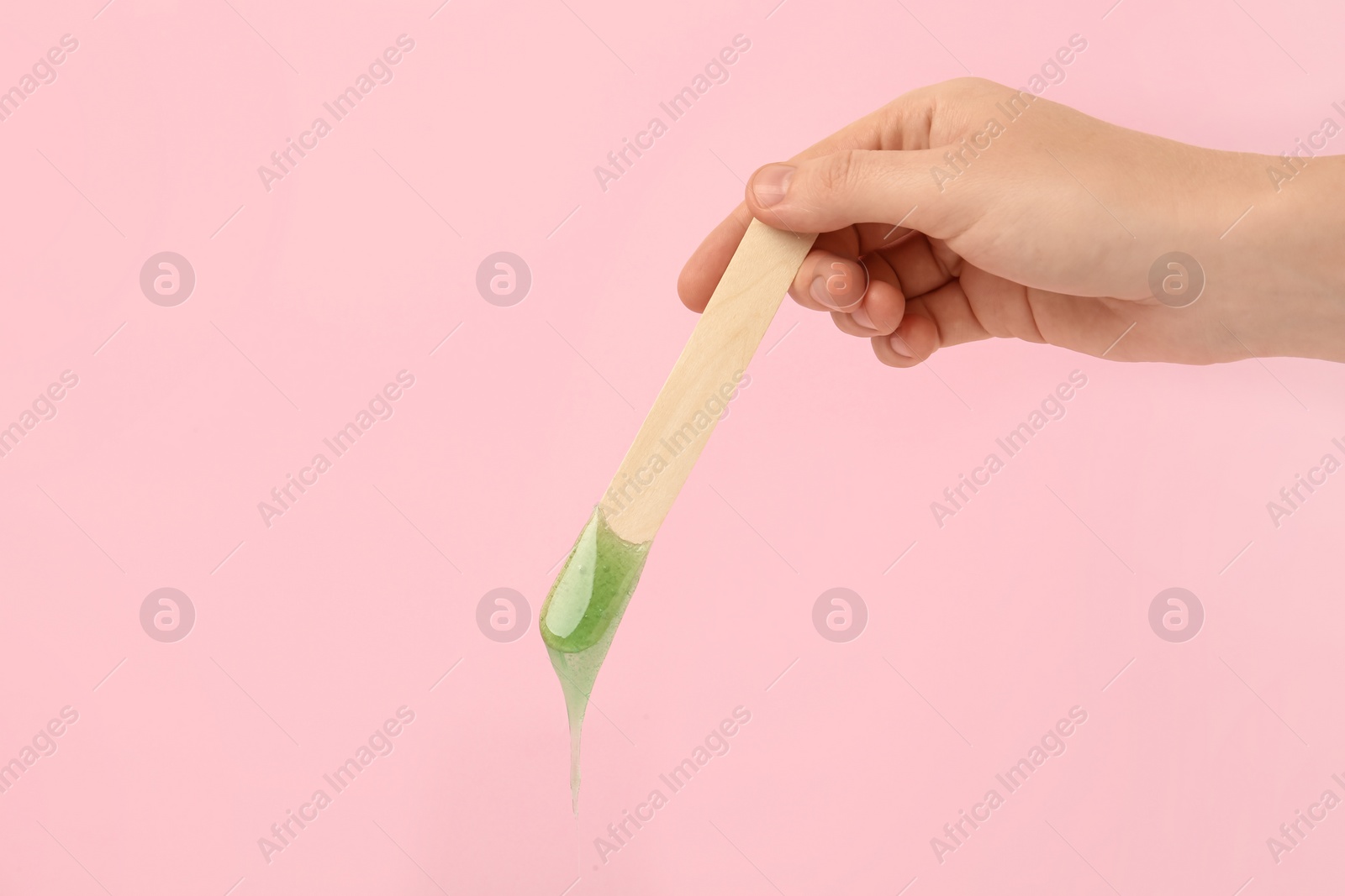 Photo of Woman holding spatula with hot depilatory wax on pink background, closeup