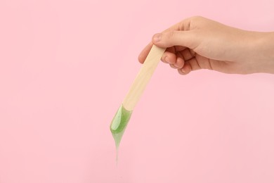 Photo of Woman holding spatula with hot depilatory wax on pink background, closeup