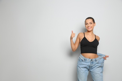 Photo of Slim woman in oversized jeans on light background, space for text. Weight loss