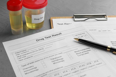 Photo of Drug test result form, containers with urine samples and pen on grey table, closeup