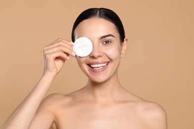 Young woman using cotton pad with micellar water on beige background