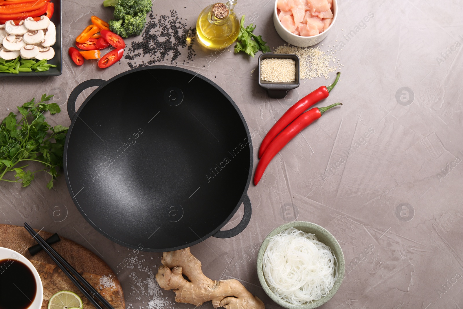 Photo of Wok, chopsticks and different products on grey textured table, flat lay. Space for text