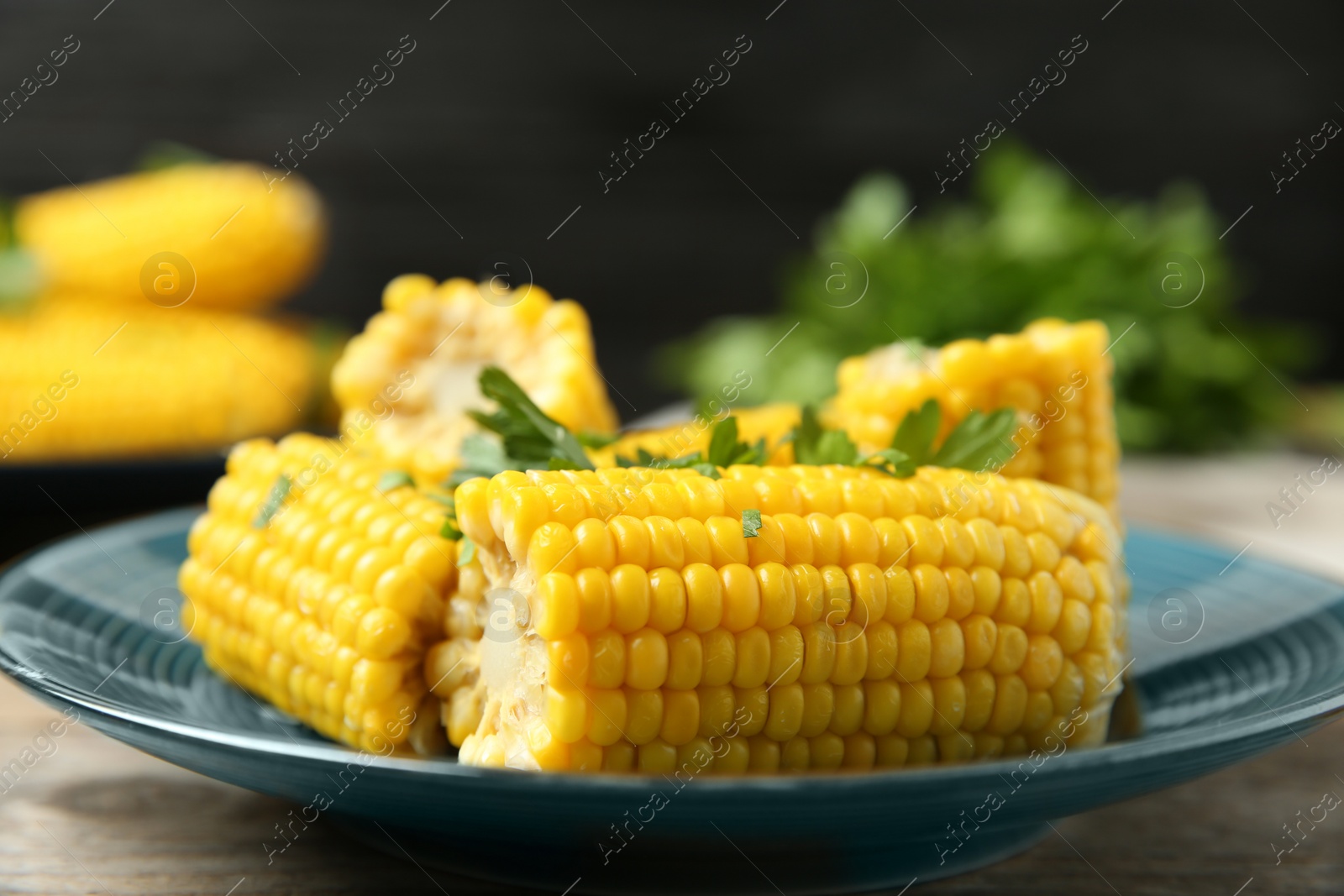 Photo of Plate of boiled corn cobs with parsley on wooden table, closeup