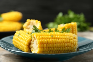 Photo of Plate of boiled corn cobs with parsley on wooden table, closeup