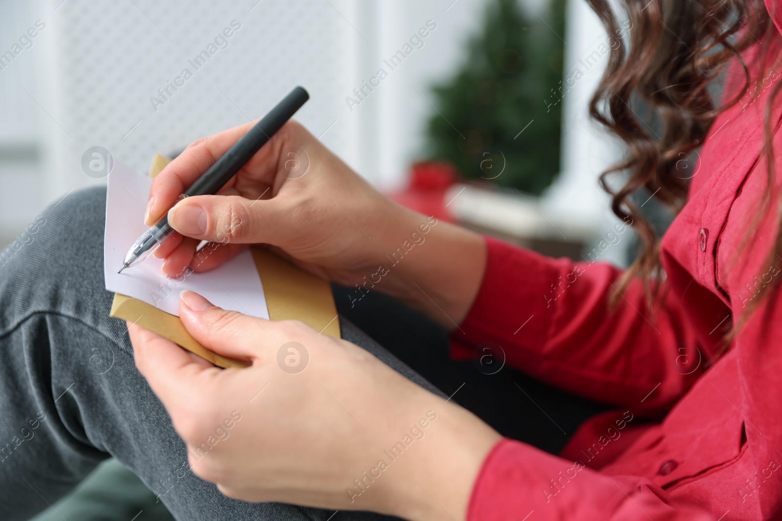 Photo of Young woman writing message in greeting card indoors, closeup