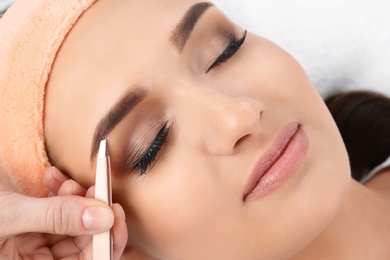 Photo of Young woman having professional eyebrow correction procedure in beauty salon