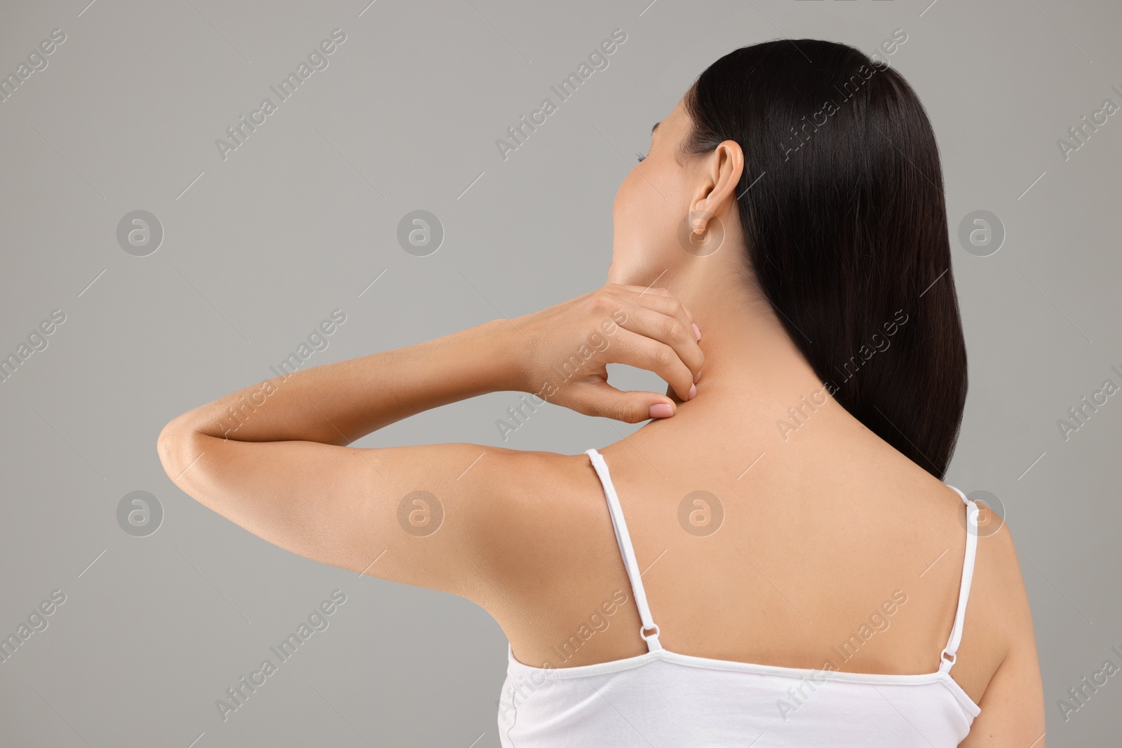 Photo of Suffering from allergy. Young woman scratching her neck on light grey background, back view