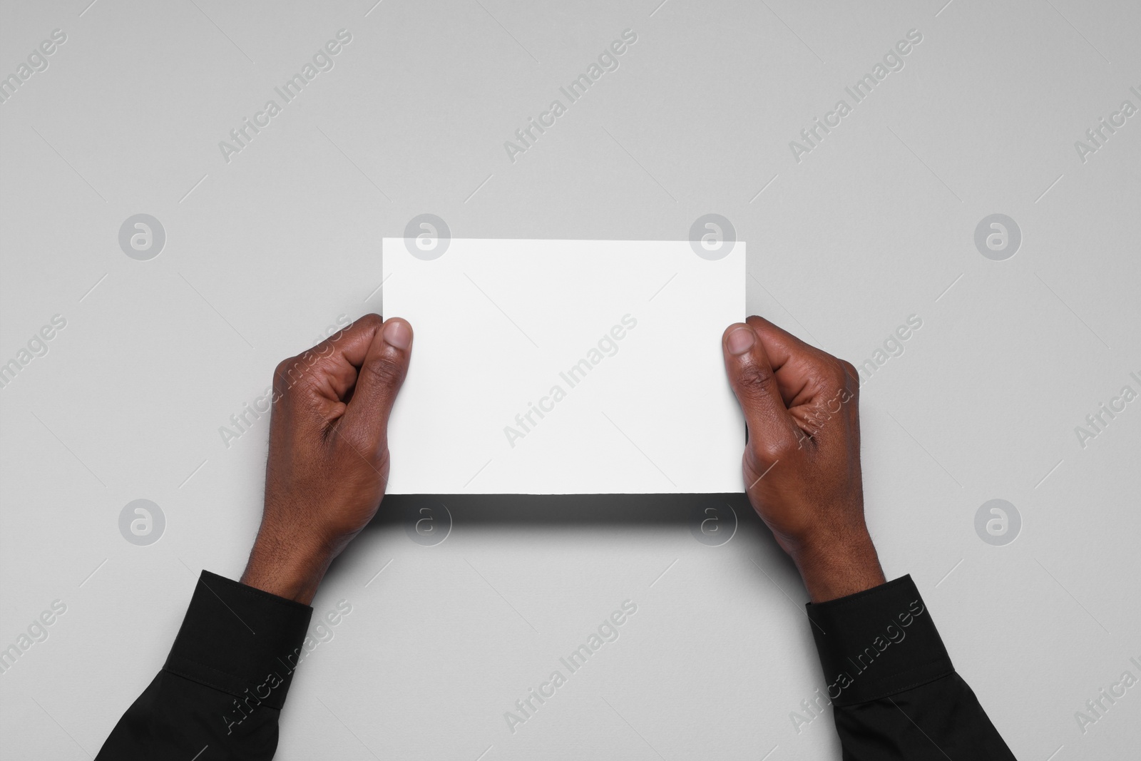 Photo of African American man holding sheet of paper on white background, closeup. Mockup for design