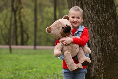 Photo of Cute little girl with teddy bear outdoors. Space for text