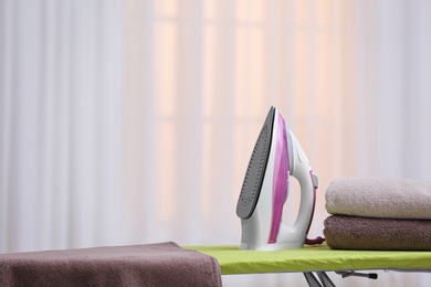 Photo of Modern iron and towels on board against blurred background. Space for text