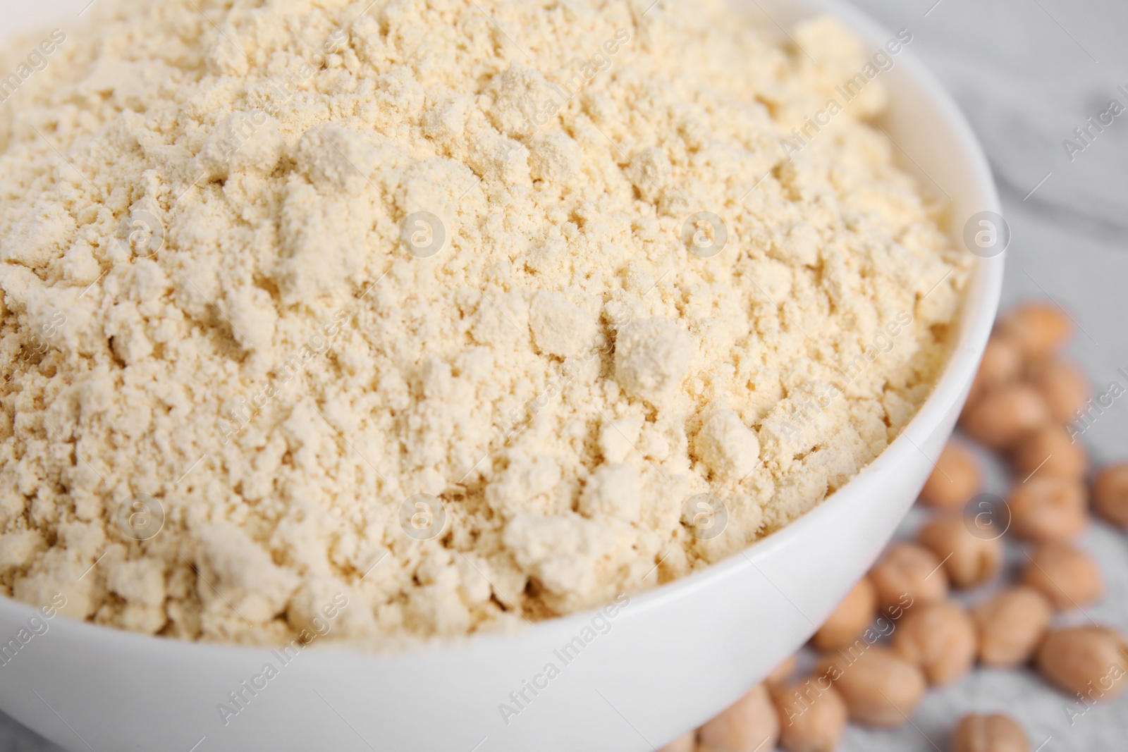 Photo of Chickpea flour in bowl and seeds on table, closeup