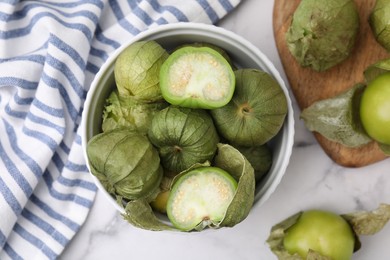 Photo of Fresh green tomatillos with husk in bowl on light marble table, flat lay