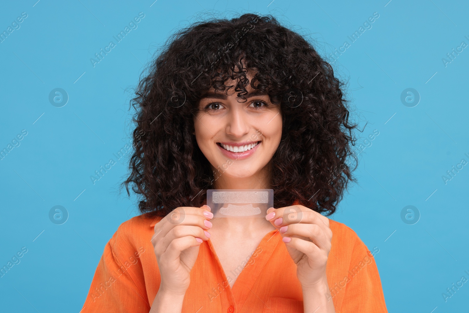 Photo of Young woman holding teeth whitening strips on light blue background