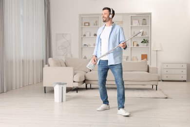 Photo of Happy man in headphones having fun with mop while cleaning at home