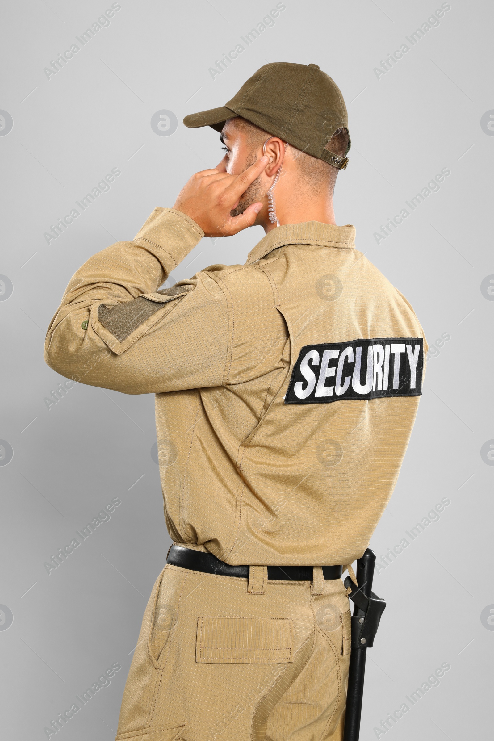 Photo of Male security guard in uniform using radio earpiece on grey background