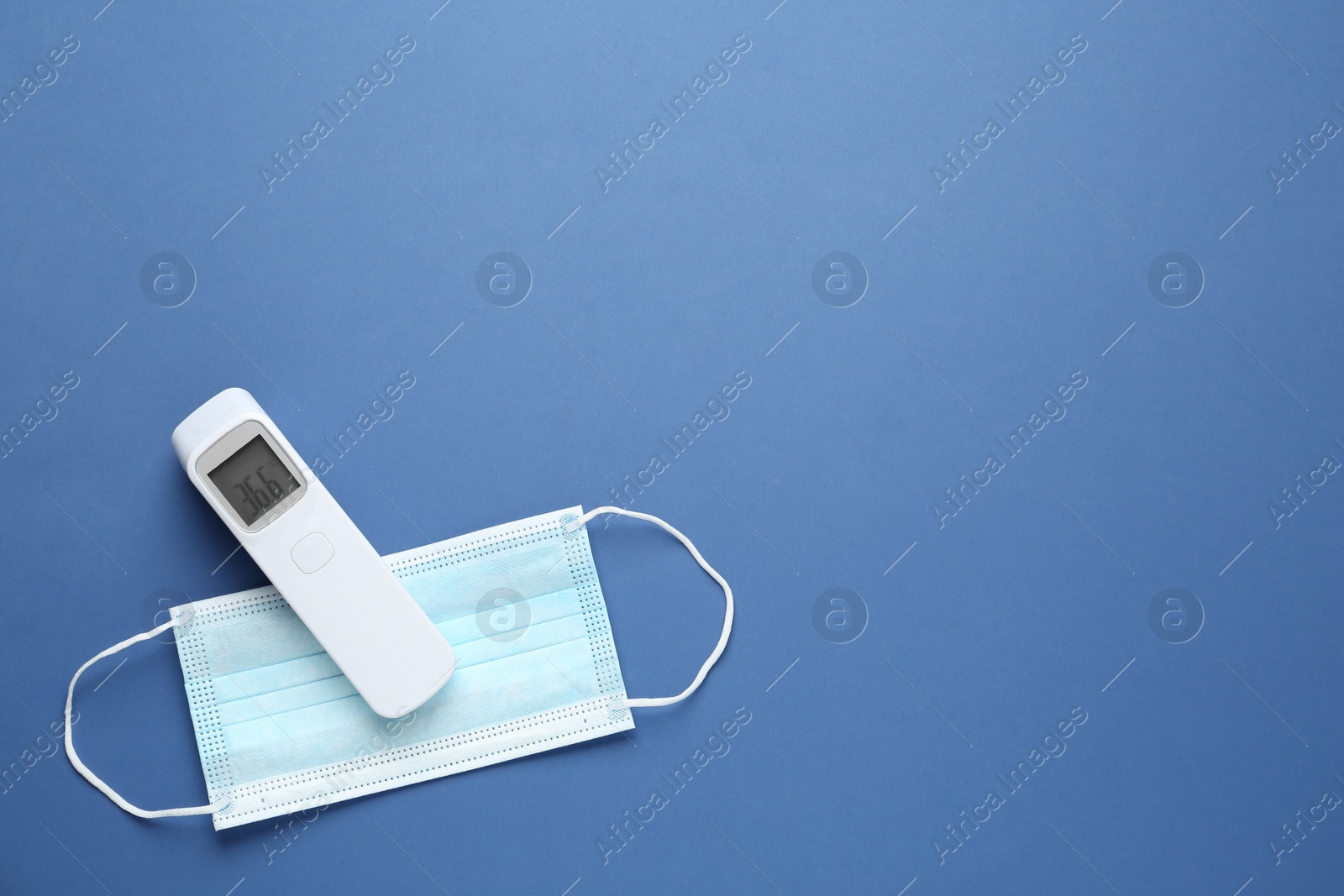 Photo of Infrared thermometer and medical mask on blue background, flat lay with space for text. Checking temperature during Covid-19 pandemic