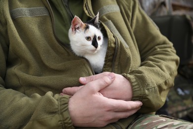 Photo of Soldier in uniform warming little stray cat, closeup