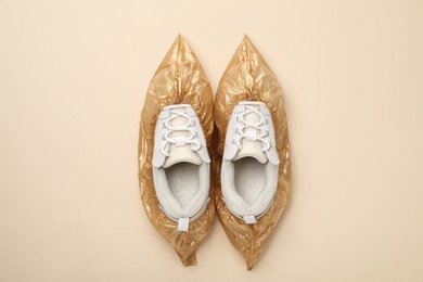 Photo of Sneakers in shoe covers on beige background, top view