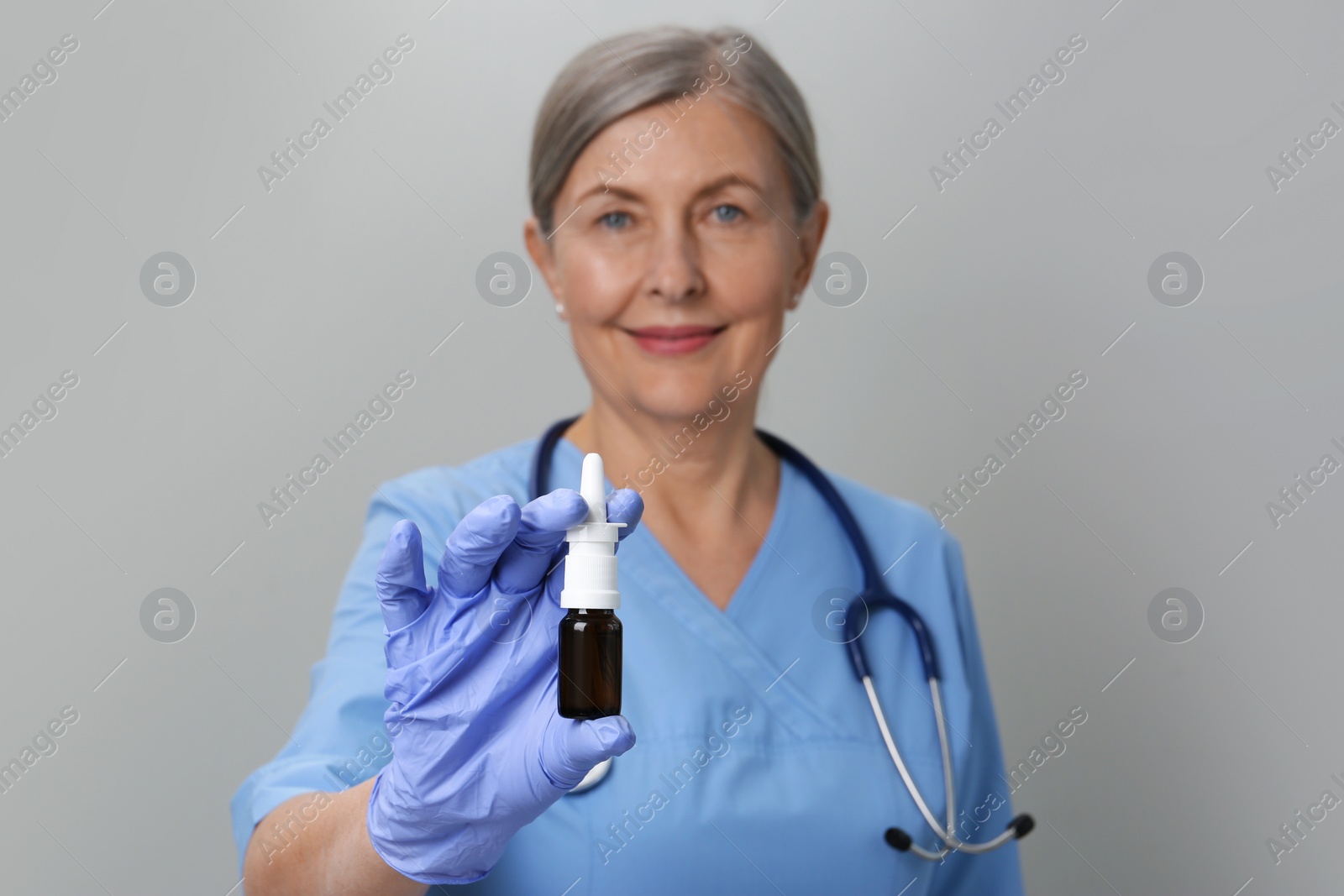 Photo of Woman holding nasal spray against light grey background, focus on bottle