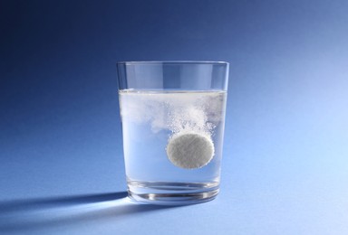 Effervescent pill dissolving in glass of water on blue background