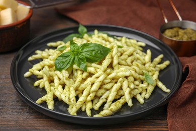 Photo of Plate of delicious trofie pasta with pesto sauce and basil leaves on wooden table