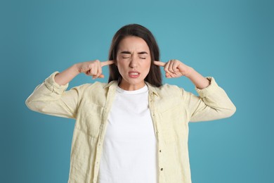 Photo of Emotional young woman covering ears with fingers on light blue background