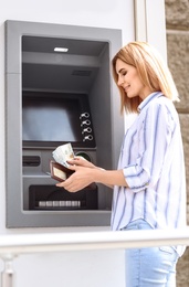 Beautiful woman with money near cash machine outdoors