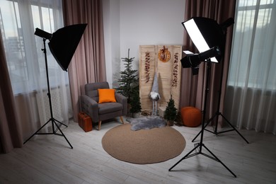 Photo of Beautiful Christmas themed photo zone with professional equipment, trees and armchair in room