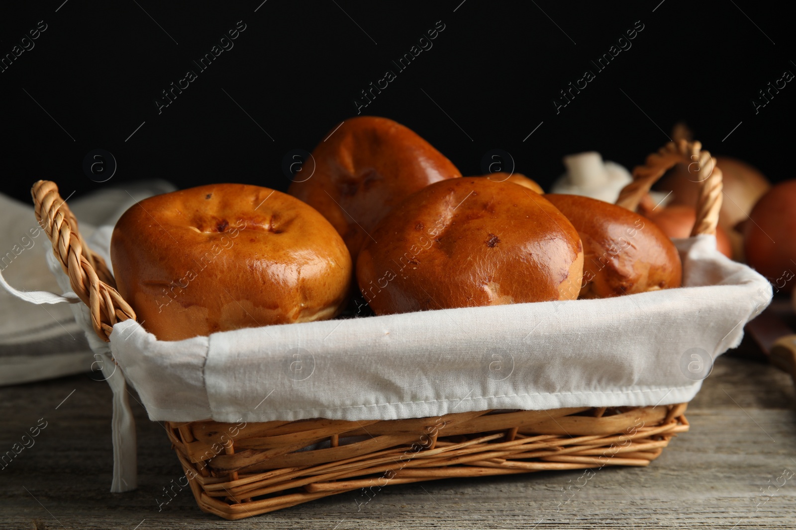 Photo of Wicker basket with delicious baked pirozhki on wooden table