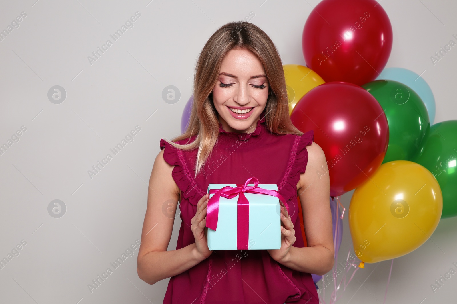 Photo of Portrait of beautiful smiling girl with gift box and air balloons on light background. International Women's Day