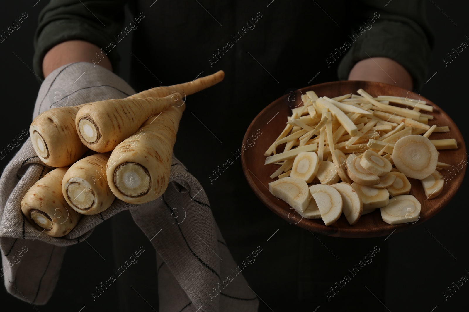 Photo of Woman holding whole and cut parsnips on black background, closeup