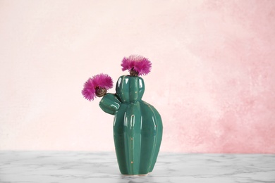 Photo of Trendy cactus shaped ceramic vase with flowers on table