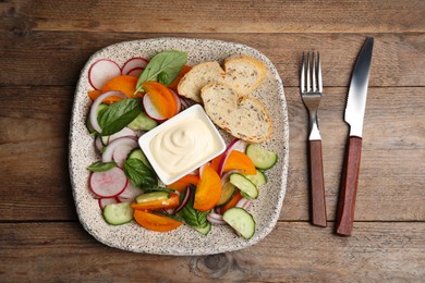 Photo of Plate of delicious vegetable salad with mayonnaise and croutons served on wooden table, flat lay