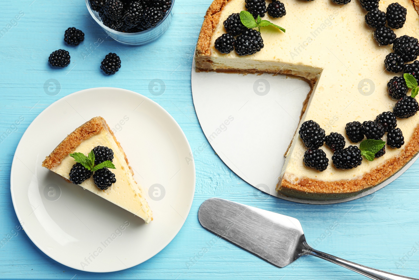 Photo of Sliced delicious cheesecake with blackberries on light blue wooden background, flat lay