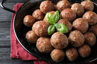 Tasty cooked meatballs with basil on black wooden table, closeup