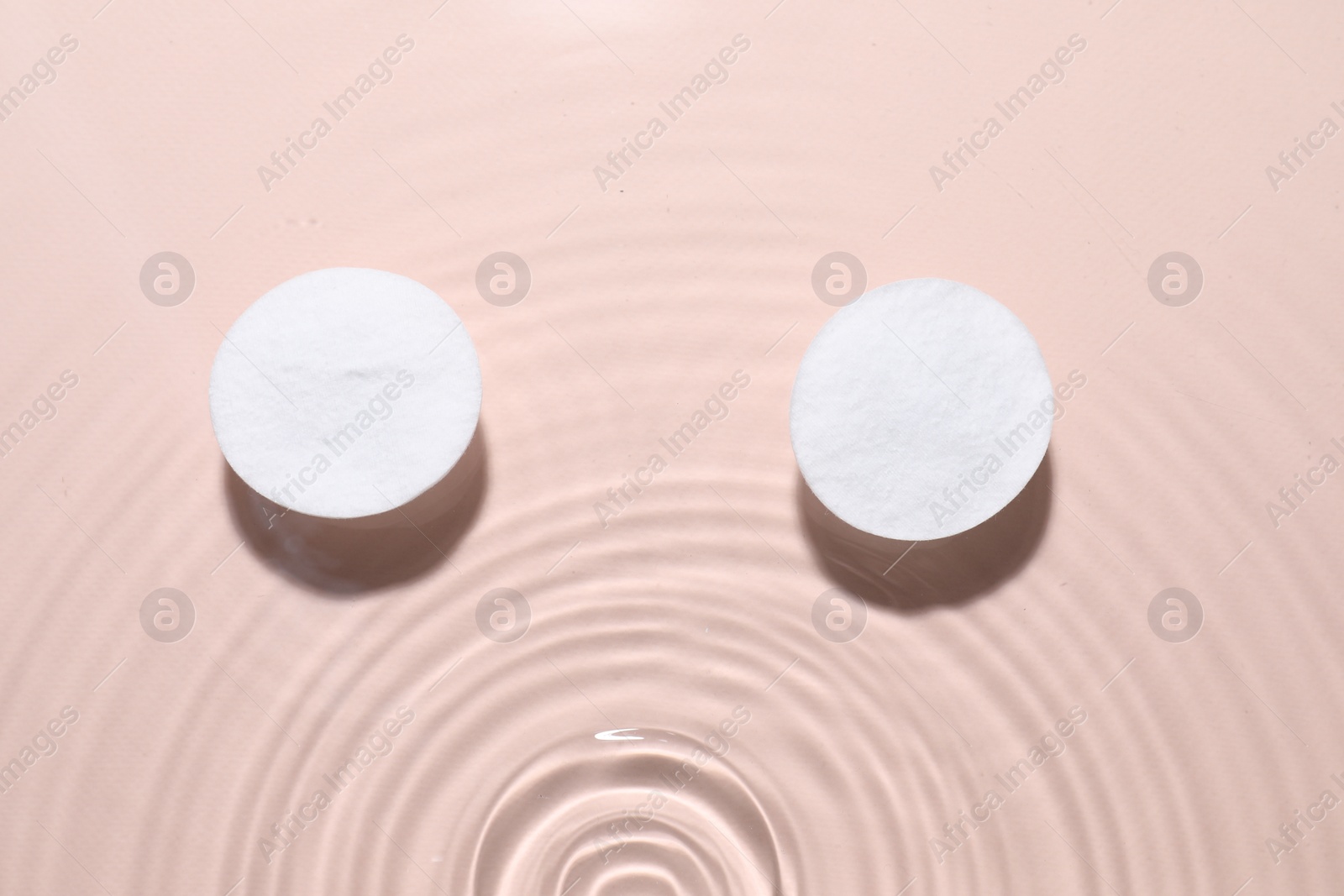 Photo of Cotton pads in micellar water on beige background, top view